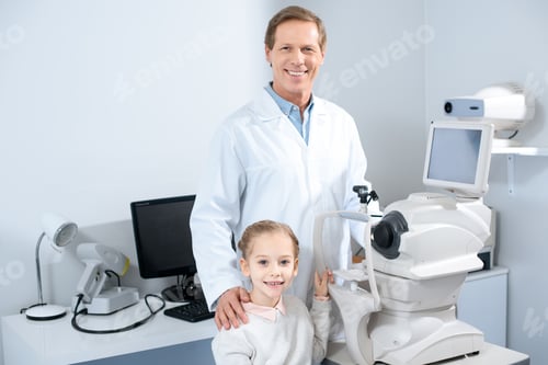 Preview: smiling ophthalmologist and pre-adolescent child looking at camera in clinic