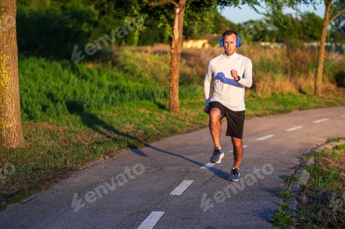 Preview: Young man wearing headphones running on the road in a park