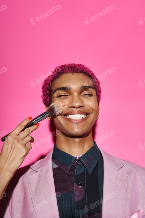 Preview: cheerful stylish male model in vivid attire smiling with closed eyes, hand with makeup brush