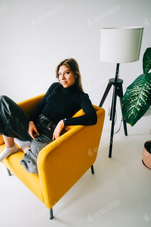 Preview: Portrait of attractive stylish caucasian young woman sitting in armchair in living room