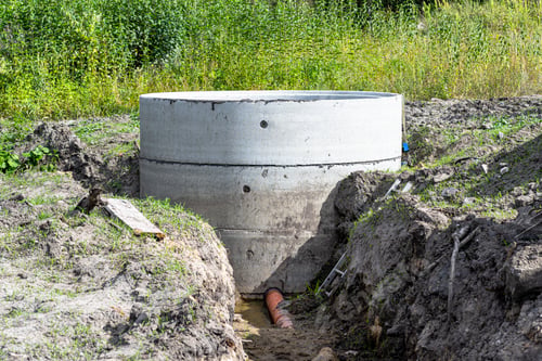 Preview: Concrete septic tank made of several rings with an orange drainpipe at the bottom.