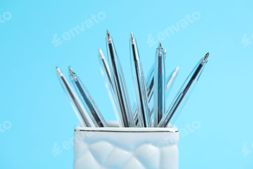 Preview: Many ballpoint pens in holder on light blue background, closeup