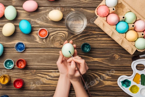 Preview: partial view of girl decorating easter eggs with paintbrush at wooden table with paints and color