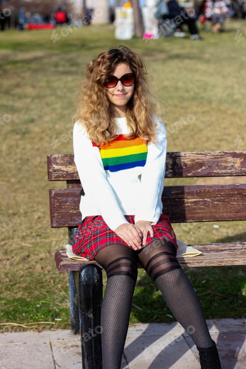 Preview: Pretty smiling teenager girl at park. Happy curly young girl wear rainbow sweater