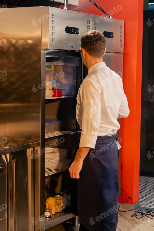 Preview: professional kitchen chef looks into the fridge and chooses ingredients for cooking food concept