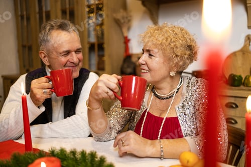 Preview: Senior couple sitting at a table by nicely decorated Christmas tree, having fun at Christmas dinner