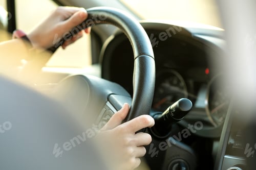 Preview: Close up view of woman hands holding steering wheel driving a car on city street on sunny day