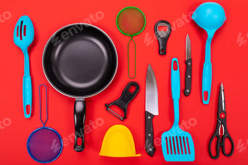 Preview: Frying pan with kitchen utensils isolated on red background