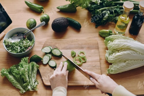 Preview: Close-up top view of unrecognizable woman cutting vegetables on the wooden desk