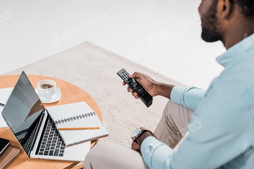 Preview: cropped view of african american man using remote controller while sitting on couch