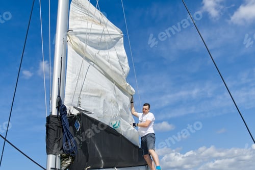 Preview: Raising the sail on a yacht. Young man captan lifting the sail of catamaran yacht during cruising