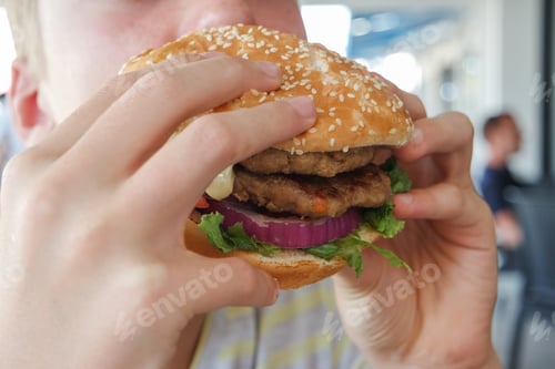 Preview: Boy eating big double hamburger.