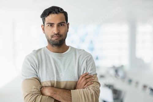 Preview: Young adult Asian man standing with arms crossed in modern open-plan office, wearing gray sweater