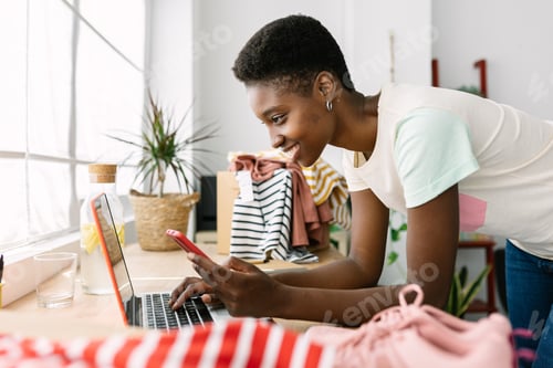 Preview: Small business african owner woman with mobile phone working on laptop in office