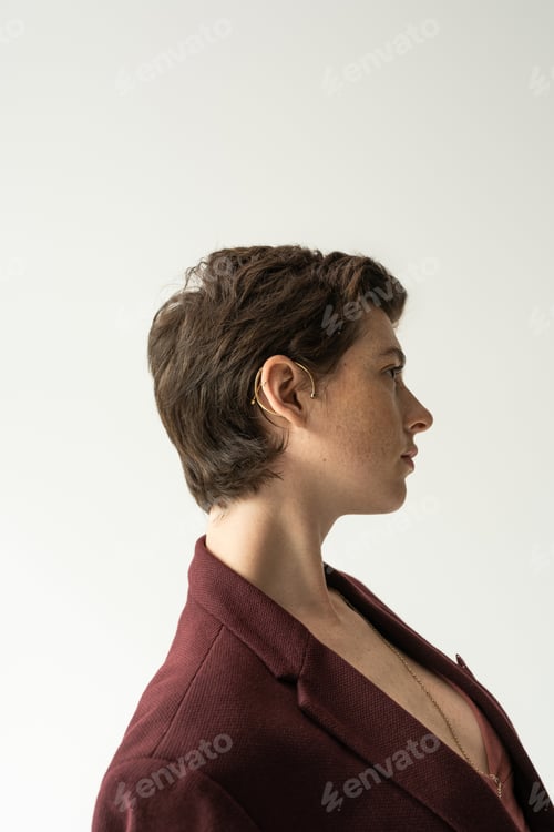 Preview: profile of stylish brunette woman in cuff earring and blazer isolated on grey