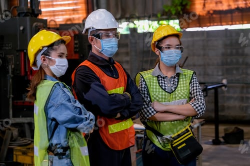 Preview: Group of man and woman workers with hygiene mask stand in confident action in the factory area.