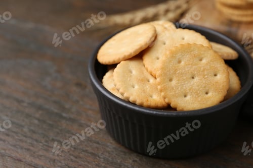 Preview: Tasty salty crackers and wheat spikes on wooden table, closeup. Space for text