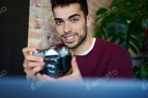 Young Man Holding Camera Indoors near Plant