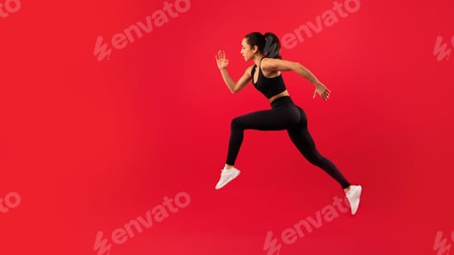 Preview: Fit woman in sportswear leaps energetically against vibrant red background