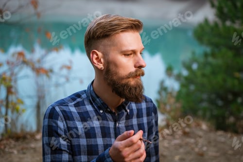 Preview: Smoking bearded man outdoors near lake in the evening. Bad habit, addiction
