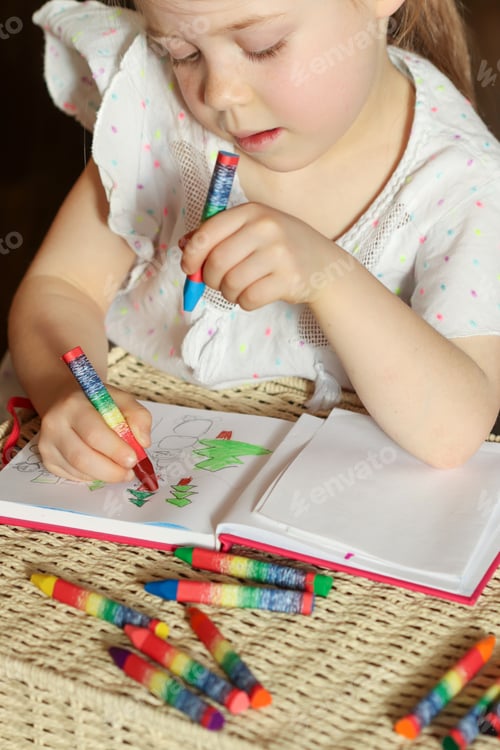 Preview: Little girl 6 years old draws with wax crayons in a sketch book