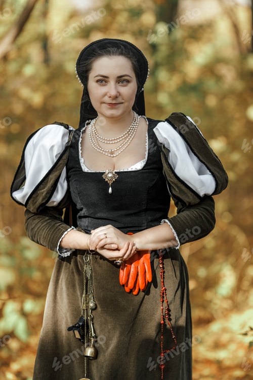 Preview: Young woman in medieval dress and cloak standing by tree in forest. Middle Ages