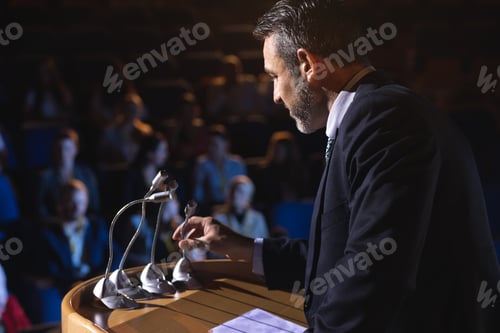 Preview: Side view of Caucasian businessman holding podium speaker in his hand at auditorium