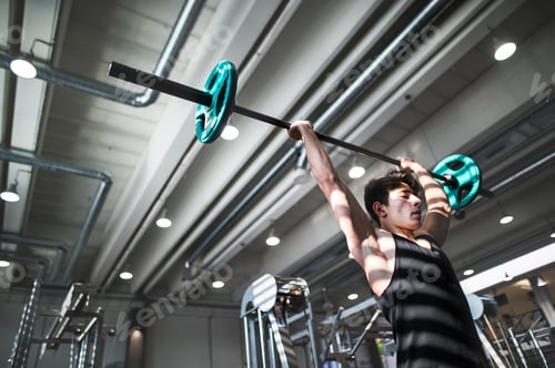 Preview: Fit young man in gym working out, lifting barbell. Copy space.