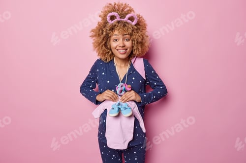Preview: Happy young pregnant European woman poses with future baby clothes dressed in pajama prepares to