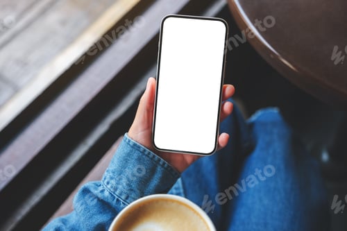 Preview: Top view mockup image of a woman holding mobile phone with blank screen and coffee cup in cafe