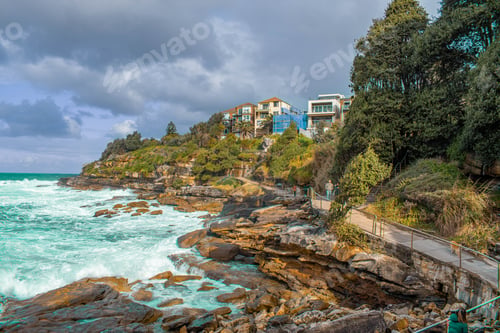 Preview: View of ocean waves hitting a rocky coast with houses in the background on a cloudy day