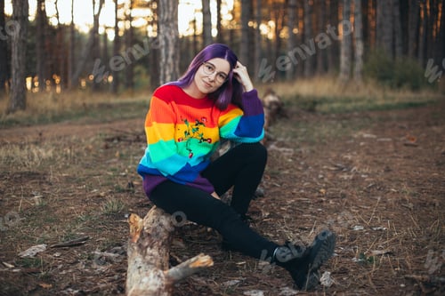 Preview: Young woman hipster with purple hair wearing glasses and colorful sweater in an autumn forest.