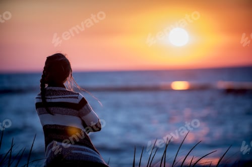 Preview: Shallow focus shot from behind of a female looking at the sea at sunset