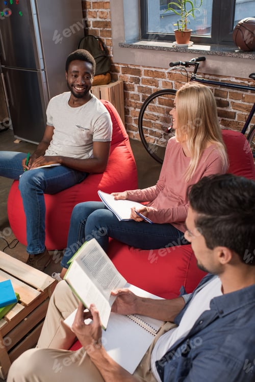 Preview: smiling multiethnic students with books studying together at home