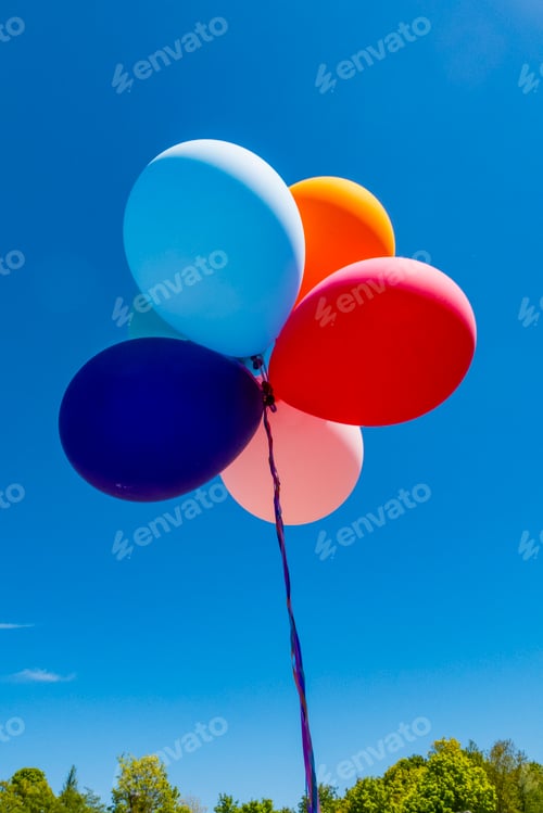 Preview: A bunch of colorful balloons inflated floating on a string, against a blue sky.