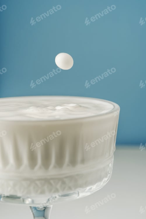 Preview: Milk pours into a beautiful crystal glass on a blue background and splashes around