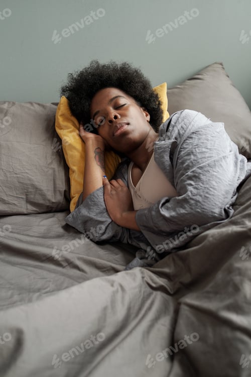 Preview: Tired African woman lying under blanket in bed
