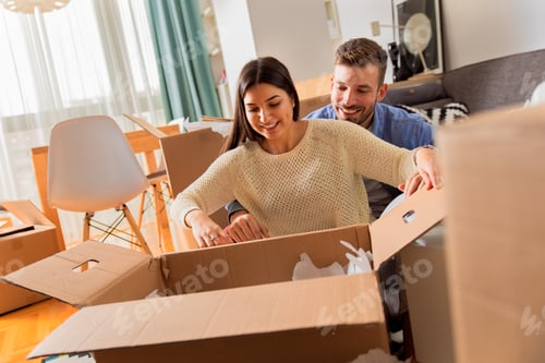 Preview: Smiling young couple move into a new home sitting on floor and unpacking.