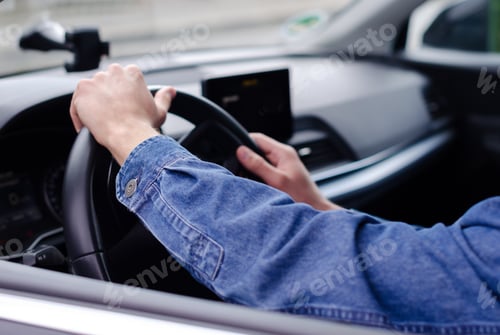 Preview: Man's hands on the steering wheel of a car, man wearing a denim shirt.