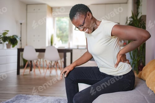 Preview: Young woman sitting on sofa at home suffering from back pain