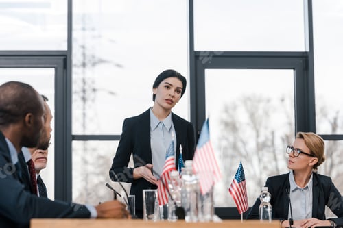 Preview: selective focus of attractive speaker talking near multicultural diplomats and american flags