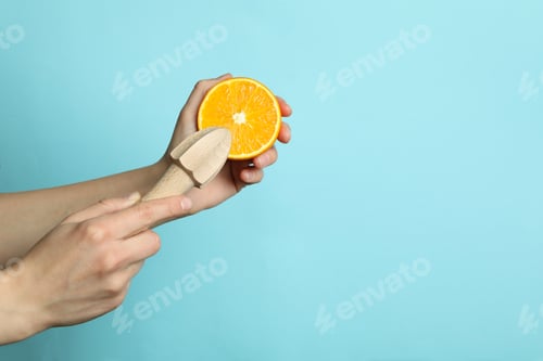 Preview: Female hands hold orange and juicer on blue background