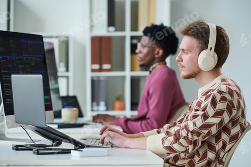 Preview: Young Man Wearing Headphones Working on Computer Beside Black Man