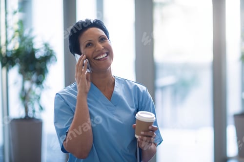 Preview: Mature African American woman smiling and speaking on smartphone in hallway, holding coffee cup