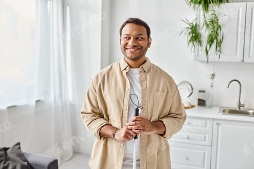 Preview: cheerful blind indian man in casual comfy attire using his walking stick and smiling happily at home