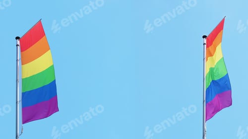 Preview: two vertical rainbow or lgbtq pride flags fly on flagpole against blue sky with copy space