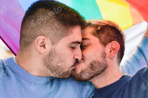 Preview: Gay male couple kissing under rainbow lgbtq flag during pride month parade