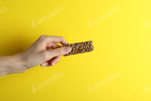 Preview: Woman holding kozinaki bar on yellow background, closeup