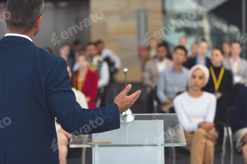 Preview: Rear view of mixed race businessman speaking at a business seminar in modern office building