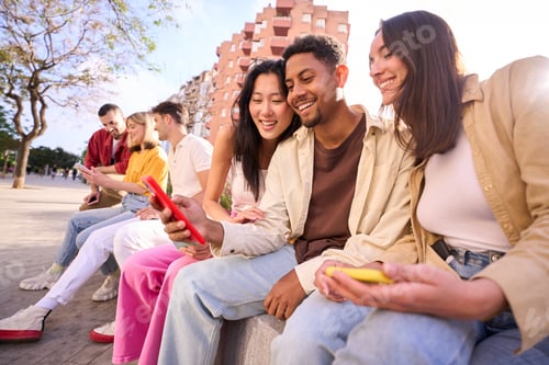 Preview: Young group of gen z people having fun using cell phone together outside.Happy community of student